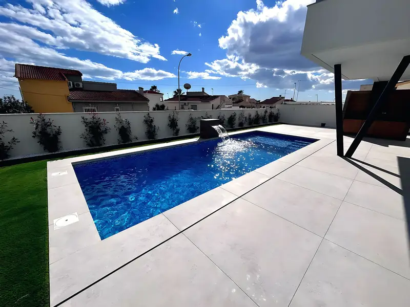 Rectangular pool with waterfall block, deep blue mosaic, light grey porcelain terrace and outdoor kitchen under a pergola