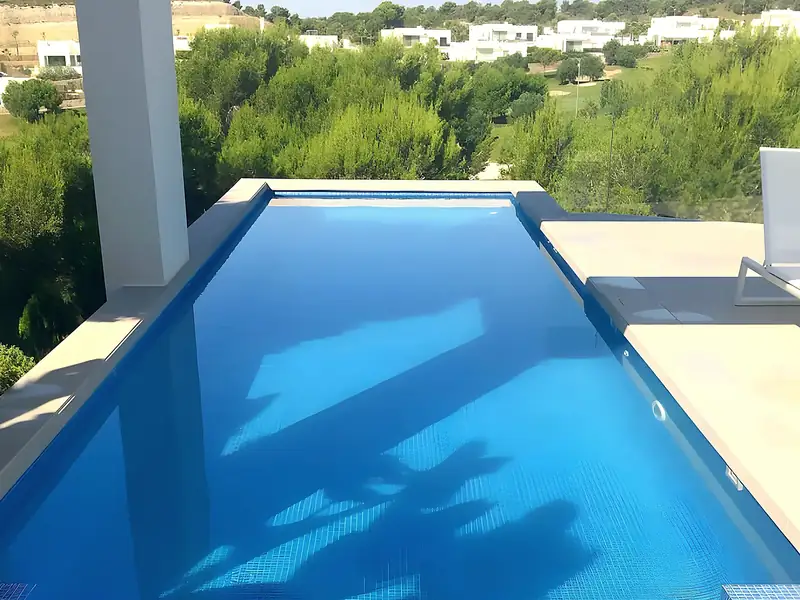 Infinity pool with deep blue mosaic, cream stone terrace and white columns over pine woodland, built by ORIGEN, Costa Blanca