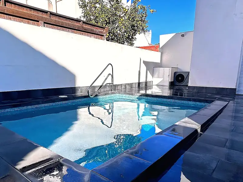 Small plunge pool with pale blue mosaic, dark glossy porcelain surround reflecting the sky, steel handrail and white walls