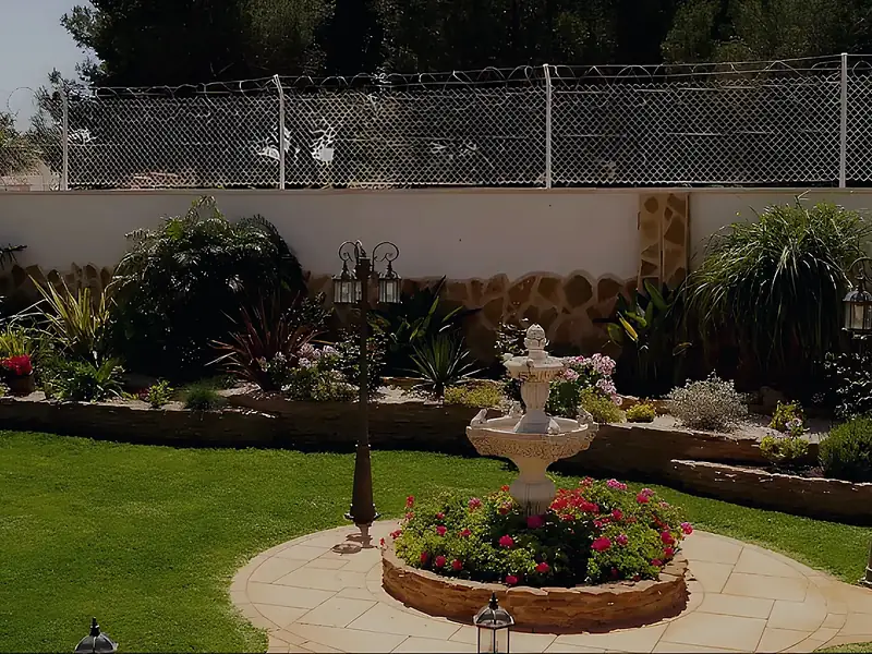 Formal garden with lawn, tiered cast stone fountain in a raised flower bed, lantern lamp posts and planted borders