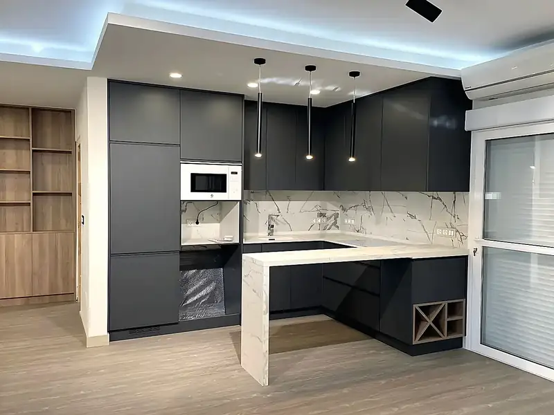 Kitchen renovation with matt dark grey handleless units, marble-effect splashback and peninsula and black pendant lights