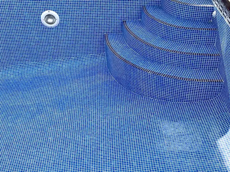 Empty pool with light blue mosaic, Greek key waterline border, curved corner steps, underwater light and dark timber deck
