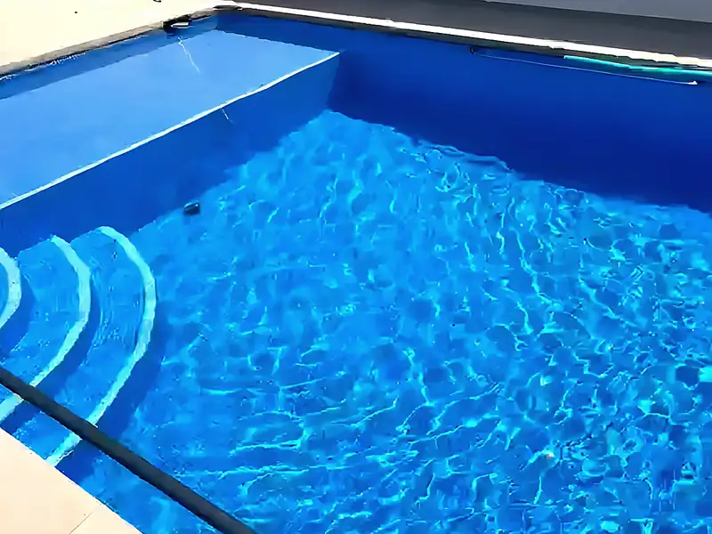 Close-up of clear rippling water in a deep blue pool with curved corner steps and a raised step in bright sunlight